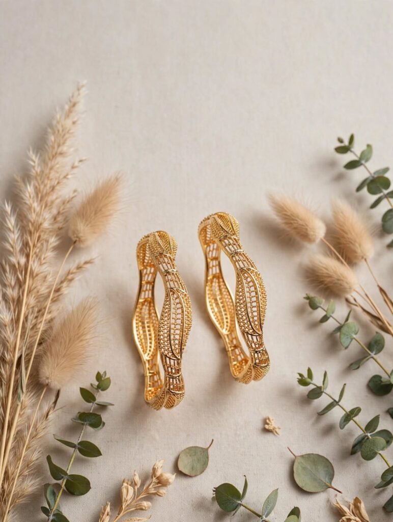 Alt Text: Wavy leaf gold plated bangles pair flat lay with pampas grass - StyleSense Pakistan